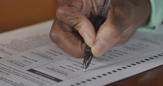 African American woman's hand filling in a voter ballot for a general election
