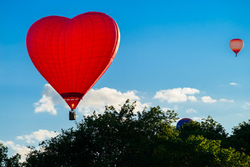 Bright red hot air balloon in the shape of heart against blue sk © smspsy