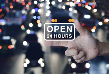 Open 24 hours icon on finger over blurred colourful night light city with cars, Business full time service concept
