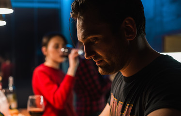 Attractive man staying near the table at home party and girl drinks wine