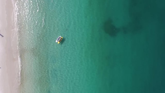 Going down slowly with the camera 90 degrees looking down between the see and sand. It is in a praia do forno beach on Arraial do Cabo. As you can see there are 2 stand up paddle boards on the water.