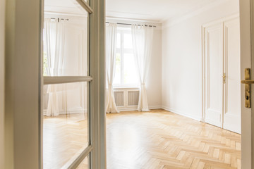 View trough door on empty white living room interior with drapes at window. Real photo
