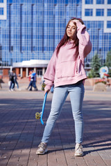 A beautiful girl with a skateboard in her hands is walking on a background of city skyscrapers.