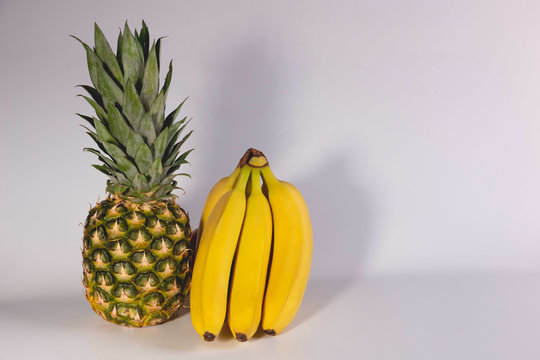 Ripe bananas and pineapple lie on white background