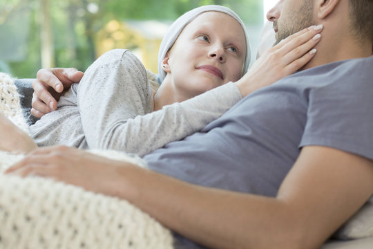 Smiling girl with cancer hugging boyfriend while relaxing at home