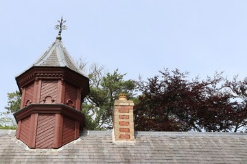 Obraz premium Old brick tower with weathervane and brick chimney stack with trees in background