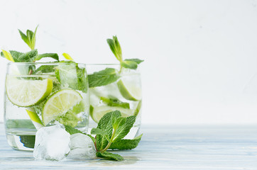 Tropical fresh cold cocktail gin tonic with mint, lime, ice, straw on light blue shabby wood board...