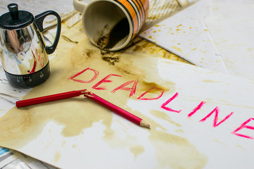 Deadline written on paper in red on the background of spilled coffee and a broken pencil.