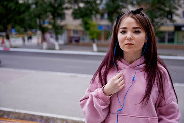cute girl with blue eyes in blue headphones listening to music from the phone. dressed in a pink sweatshot and jeans.