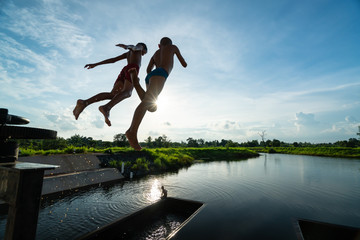 Two kids in the air while jumping into lake with nice sunray - summer nature scenery