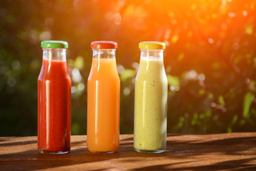 Three bottles of juice in the garden on a background of greenery. Summer, sunlight