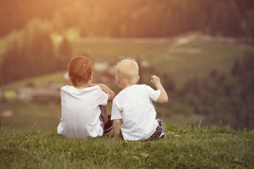 Fototapeta premium Two boys sit on the hill and talking cheerfully. Back view