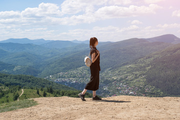 Naklejka na ściany i meble Girl with a backpack standing on the hill and admiring the view. Sunny day