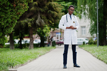 Stylish african american doctor with stethoscope and lab coat, at glasses posed outdoor.