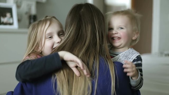 Happy children hugging their mother in the bedroom.