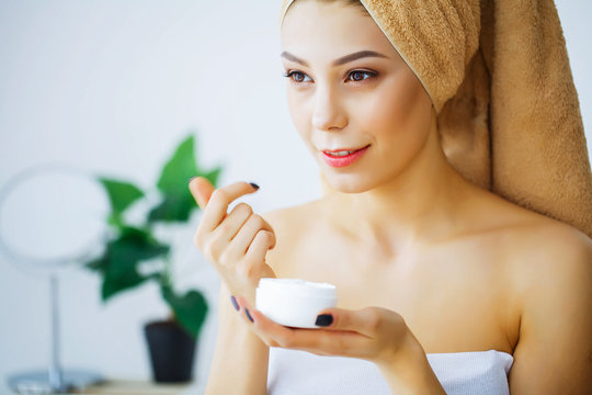 Beauty and Care. Young Woman with Cream for Face in Hands. Girl with a towel on the head. Morning Skin Care. High Resolution