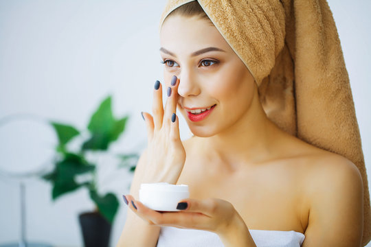 Beauty and Care. Young Woman with Cream for Face in Hands. Girl with a towel on the head. Morning Skin Care. High Resolution