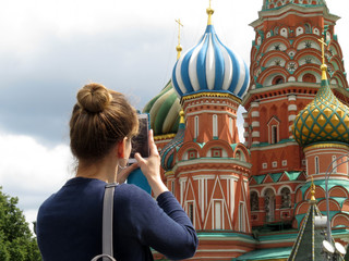 Woman tourist taking pictures with smartphone the St. Basil's cathedral on Red square in Moscow....