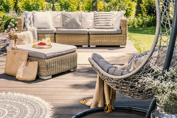 Pillows on rattan couch and table on patio with hanging chair during summer. Real photo
