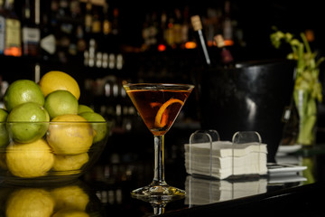 Closeup glass of Manhattan cocktail decorated with orange twist at bar counter background.