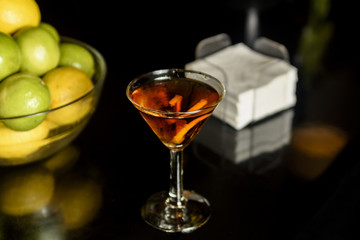 Closeup glass of Manhattan cocktail decorated with orange twist at bar counter background.