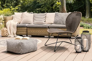 Foto op Canvas Patterned pouf and rattan chair on wooden patio with pillows on sofa and lanterns. Real photo © Photographee.eu