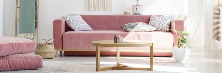 Horizontal photo of a feminine living room interior with a pink sofa, pillows, coffee table, poufs...