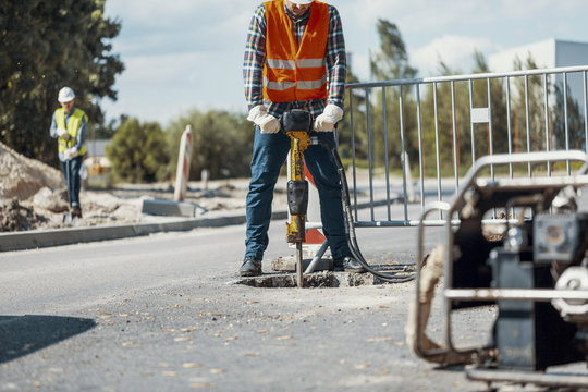 Worker with a pneumatic hammer breaking asphalt at road construction site