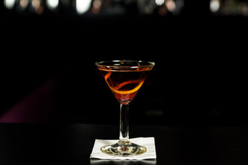 Closeup glass of Manhattan cocktail isolated decorated with orange twist at bar counter background.