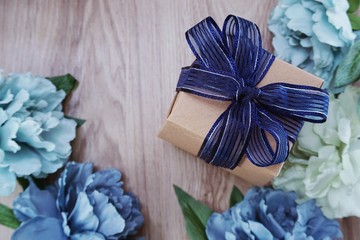 top view of gift box present with blue ribbon and  flower bouquet on space wooden background