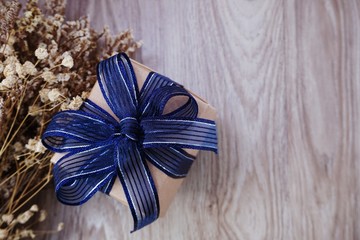 top view of gift box with blue ribbon and dried flower on space wooden background