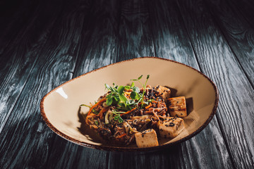 close up view of soba with tofu and vegetables decorated with germinated seeds of sunflower on plate on wooden table