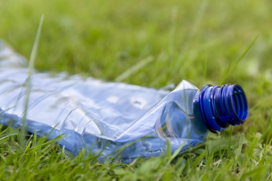 Crushed blue plastic bottle laying in grass. Pollution and environment concept