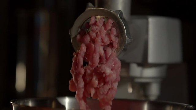 Close up shot of electic meat mincer mincing raw meat in the kitchen. Mincing meat for the cooking. Gears spinning.