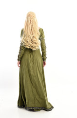 full length portrait of blonde girl wearing green medieval gown, standing pose facing away from...