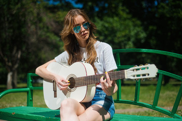 Fototapeta na wymiar Beautiful young hipster girl playing guitar outdoors in the Park