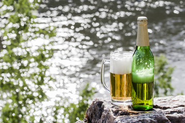 Bottle and mug of beer stands on a rock at the river