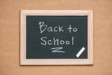 Fototapeta premium top view of blackboard with back to school inscription and piece of chalk on brown background