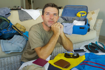 Fototapeta premium young attractive and happy man at home couch preparing travel back and suitcase folding clothes and organizing passport and things excited