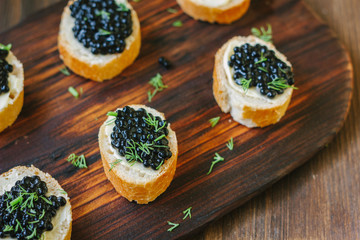 Black caviar on the pieces of bread over wooden kitchen board.