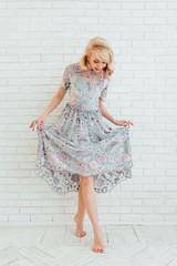 Blonde happy woman in light dress with stay in front of light wall
