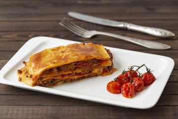 Tasty lasagna with meat covered with cheese, served with baked tomatoes on a white plate.