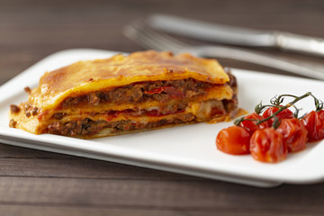 Tasty lasagna with meat covered with cheese, served with baked tomatoes on a white plate.