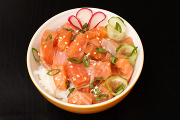 Hawaiian poke with salmon and sesame seeds, boiled rice, fresh cucumber, radish and green onions in porcelain bowl