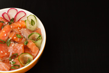 Hawaiian poke with salmon and sesame seeds, fresh cucumber, radish and green onions in porcelain bowl