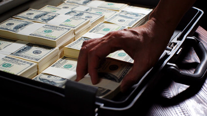 Men packing 100 US dollar bills in to briefcase