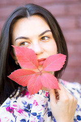 Pretty Girl hiding behind red autumn leaf a brick wall background