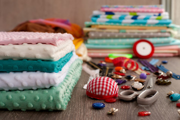 The plush fabric is folded. Plush fabric of different colors is stacked. Fabric for sewing clothes and other items. Needles, scissors cloth, buttons are needed for tailoring. 