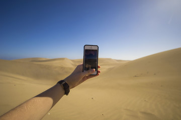 Maspalomas Dunes, Gran Canaria, Canary Islands, Spain, view of sunset dunes, wind is taking the sand over, woman hand holding smartphone and taking pictures