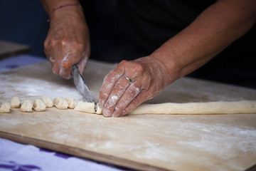 The hands of an elderly woman cut the dough into small pieces. Making Donuts